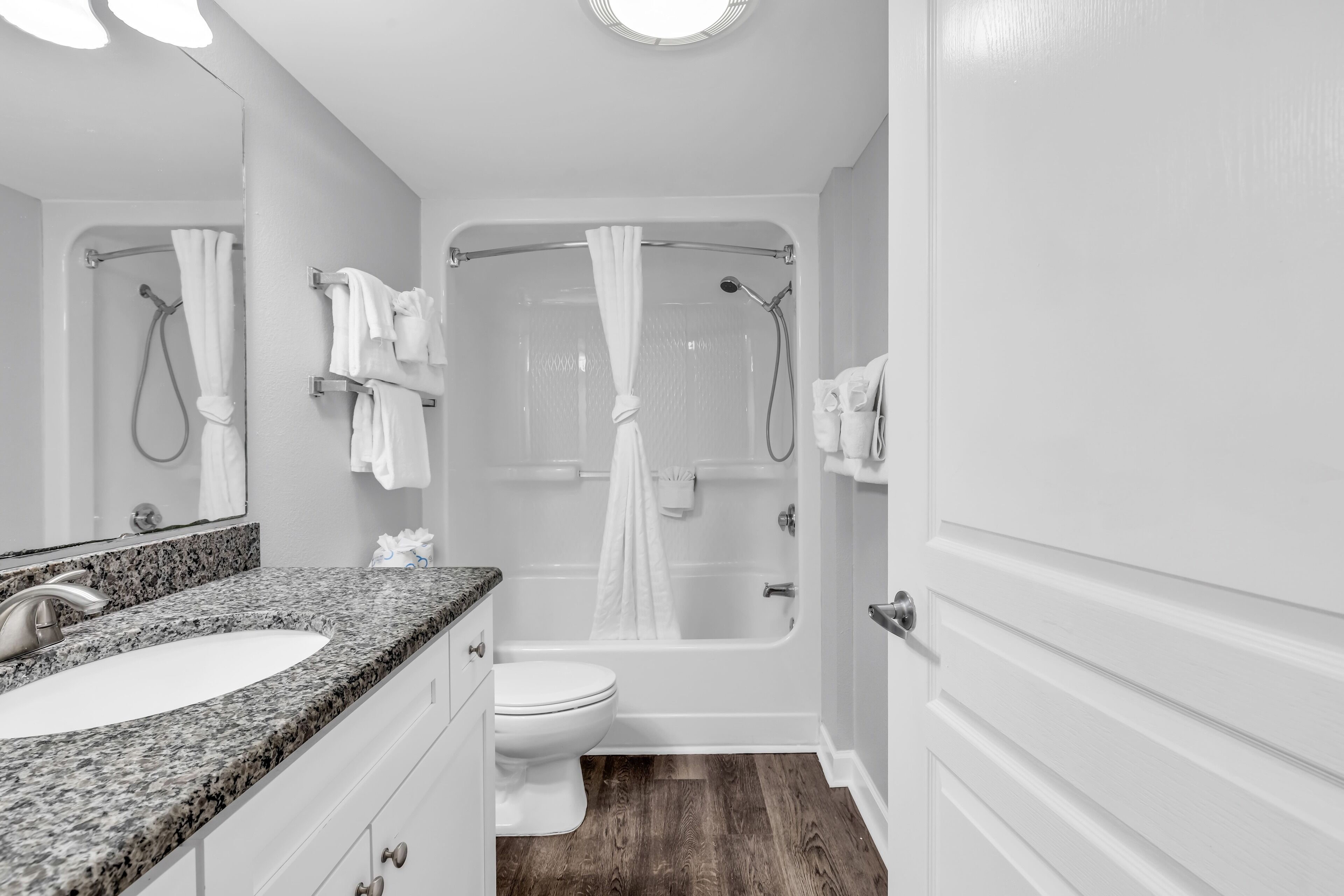 A bathroom with a granite countertop sink, a toilet, a bathtub with a showerhead, and a mirror.