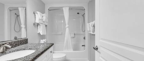 A bathroom with a granite countertop sink, a toilet, a bathtub with a showerhead, and a mirror.