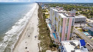 Een strandhotel met meerdere verdiepingen, een zwembad en een parkeerplaats.