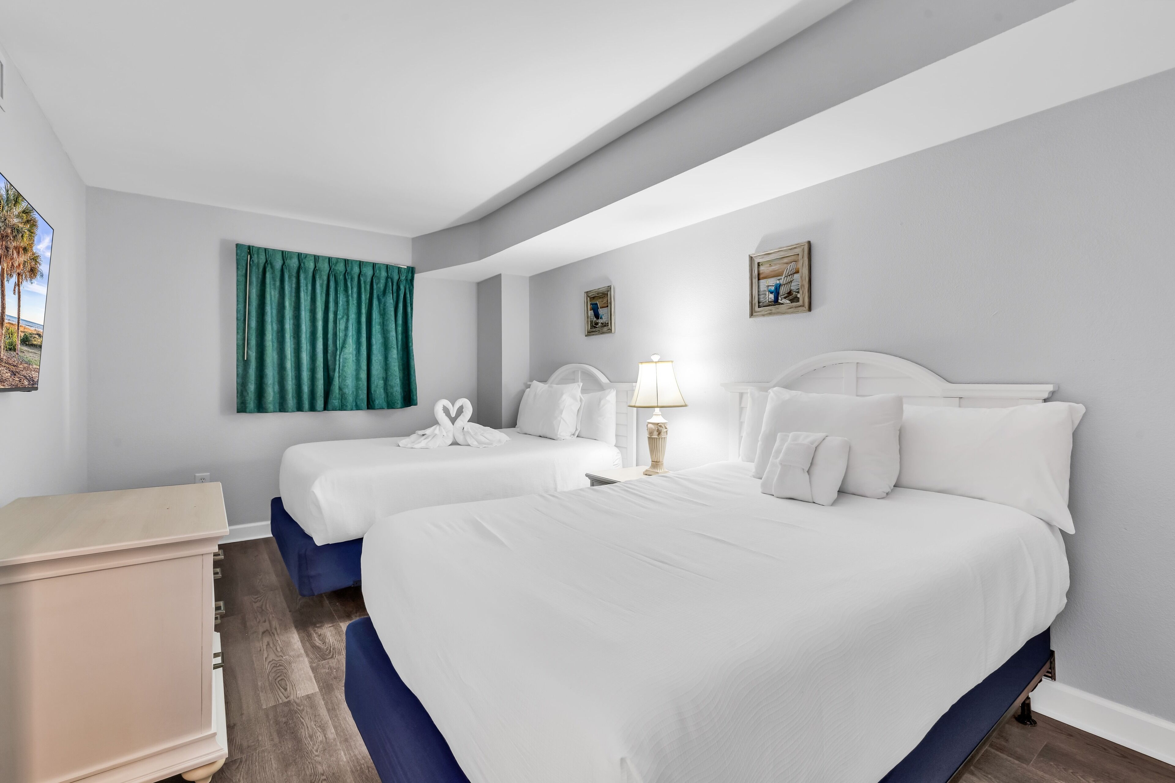 A hotel room with two beds, a dresser, a lamp, and a painting on the wall.