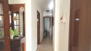 Un pasillo con una puerta de madera a la derecha, un espejo a la izquierda y suelo de baldosas.