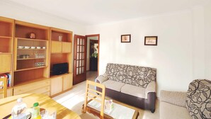 Una sala de estar con un sofá, una mesa de centro y un televisor. Se observan armarios de madera con puertas de vidrio y una puerta que da a otra habitación.