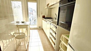 Una cocina con armarios blancos, horno negro y ventana que deja entrar luz natural.
