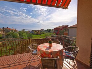 A balcony with a table and chairs, a view of a green landscape, and houses in the background. - Bright Apartment With Garden and Balcony (Vodnjan)