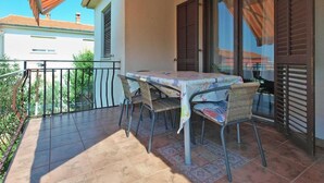 Een balkon met een tafel en stoelen, een betegelde vloer en uitzicht op omliggende gebouwen.