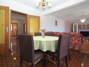 A dining area with a round table, chairs, and a vase of flowers. There is a sofa and a television in the background. - Bright Apartment With Garden and Balcony (Vodnjan)