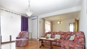 Een woonkamer met een houten parketvloer, een sofa met dessin, een fauteuil met dessin, een salontafel met een vaas, en een kroonluchter.