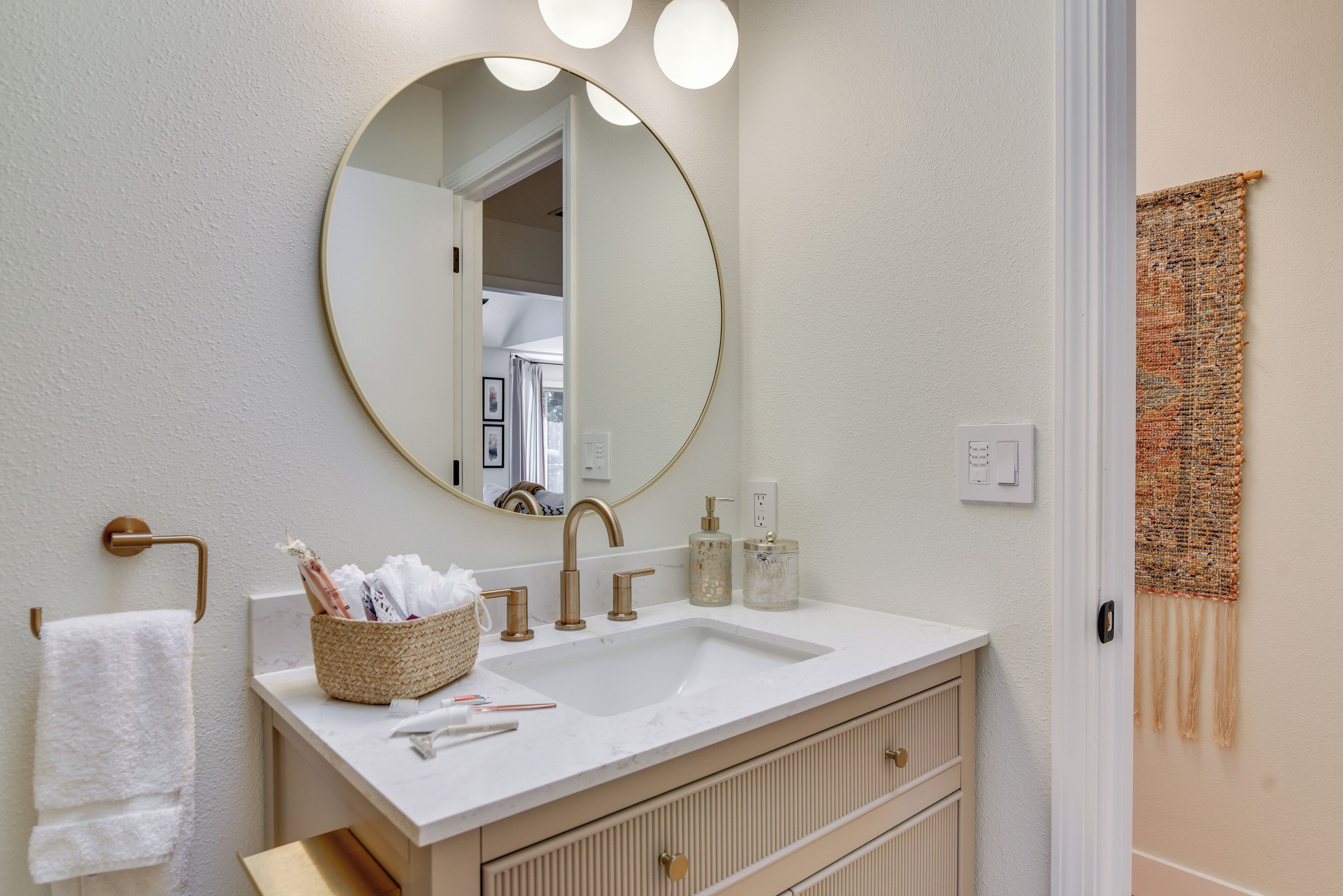 A bathroom with a white vanity, a round mirror, and a towel rack.