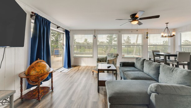 A spacious living room with a large gray sofa, a wooden coffee table, and a globe on a stand. There is a ceiling fan and a chandelier. - Family Friendly! Games! Waterfront North Port Home (North Port)