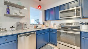 A modern kitchen with blue cabinets, stainless steel appliances, and a red pendant light. - Family Friendly! Games! Waterfront North Port Home (North Port)