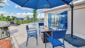 An outdoor patio with a table and chairs, a grill, and a large umbrella. - Family Friendly! Games! Waterfront North Port Home (North Port)