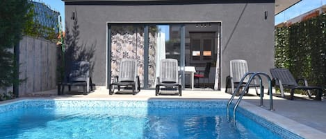 A modern outdoor pool area with a clear blue pool, lounge chairs, and a covered seating area.