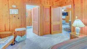 Een houten cabin met een bed, een bankje, een lamp en een deur naar een andere kamer.