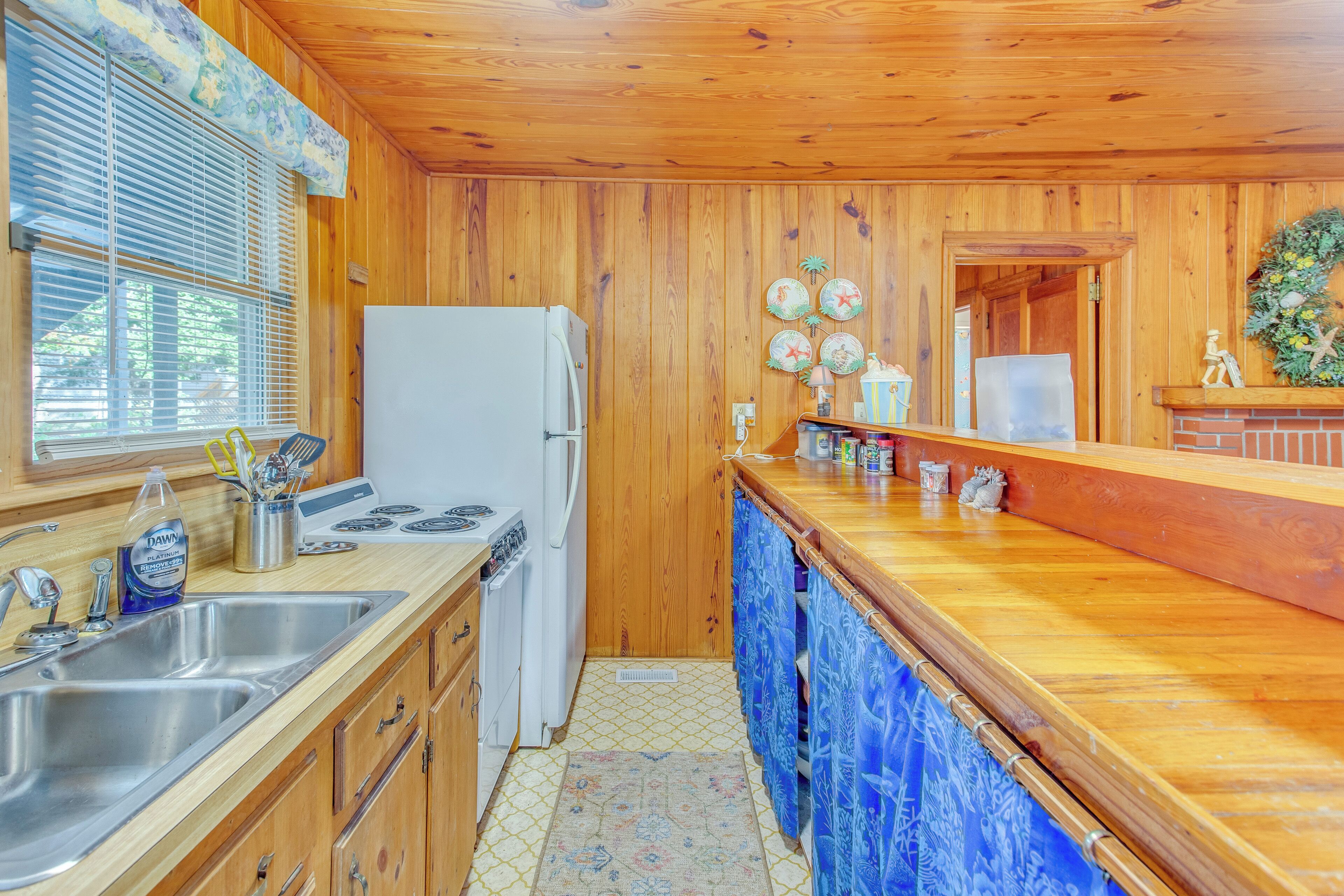 A wooden-paneled kitchen with a refrigerator, sink, and wooden countertop.