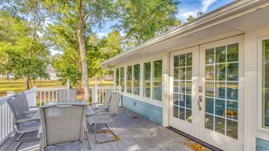Een overdekt terras met een tafel en stoelen, uitzicht op een huis achtergrond, en een houten terras.
