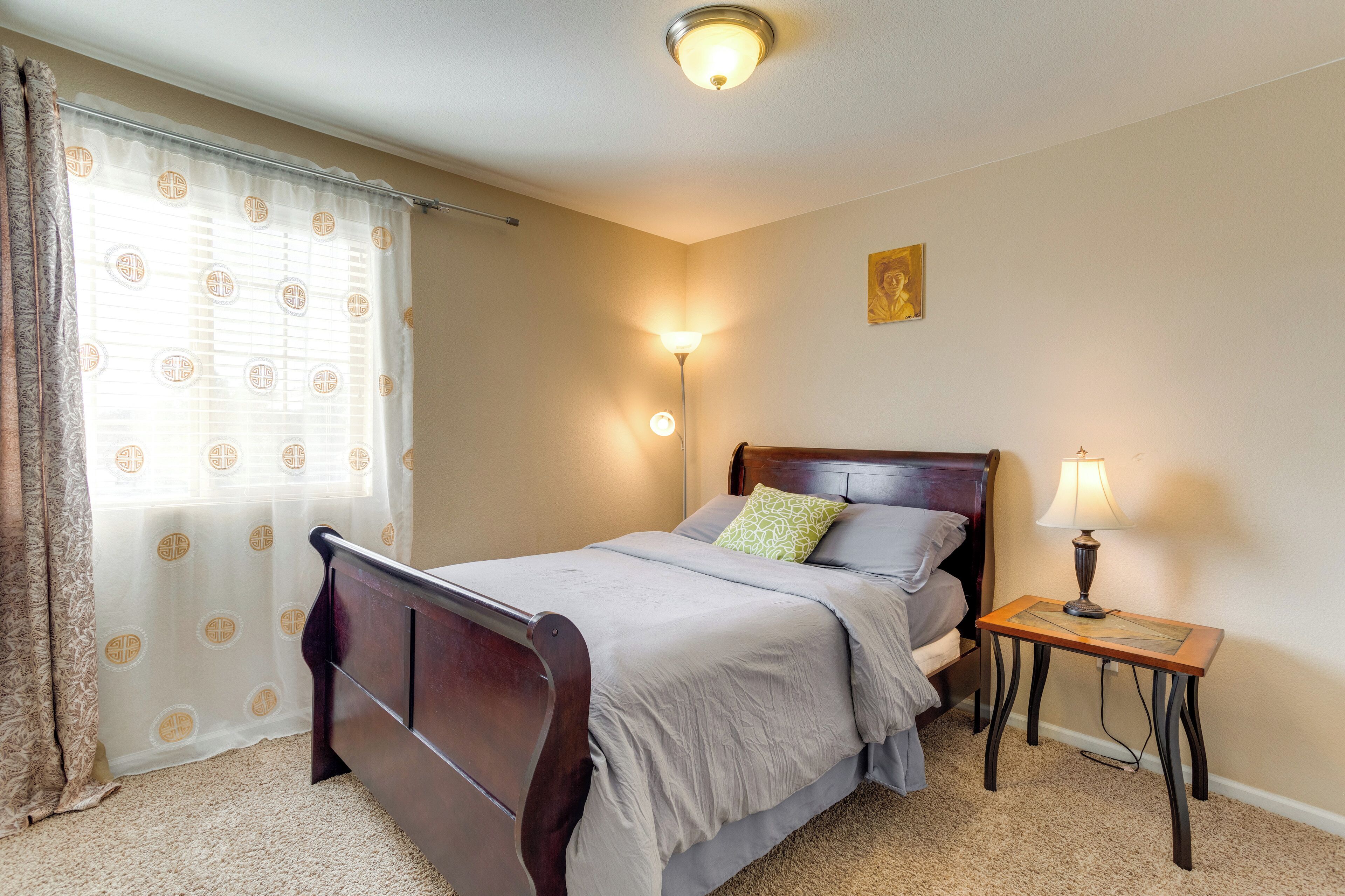 A bedroom with a wooden bed, a bedside table with a lamp, and a window with curtains.