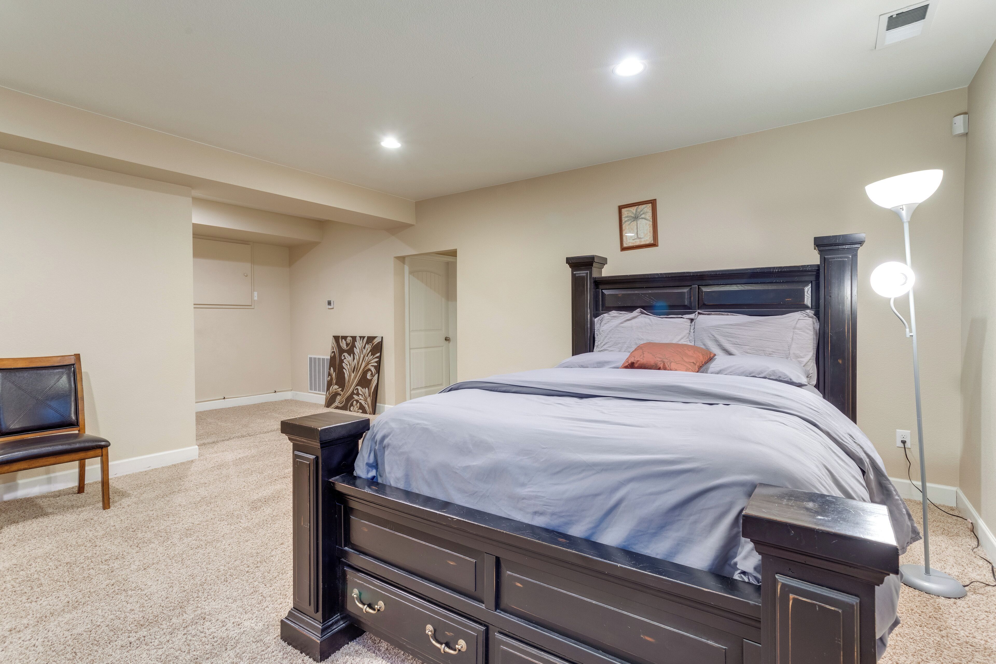 Un dormitorio con una cama de madera oscura, paredes color beige y una lámpara de pie clara.