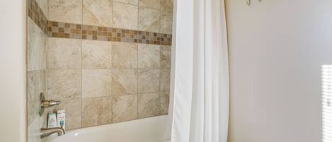 A bathroom with a bathtub, a shower curtain, a towel rack, and toiletries on the wall.