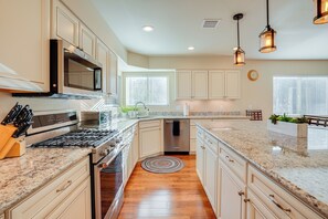 A modern kitchen with a stainless steel stove, microwave, and dishwasher. It features light-colored cabinetry, a granite countertop, and a wooden floor. - 3 Mi to Downtown Prescott - Spacious Home w/ Patio (Prescott)
