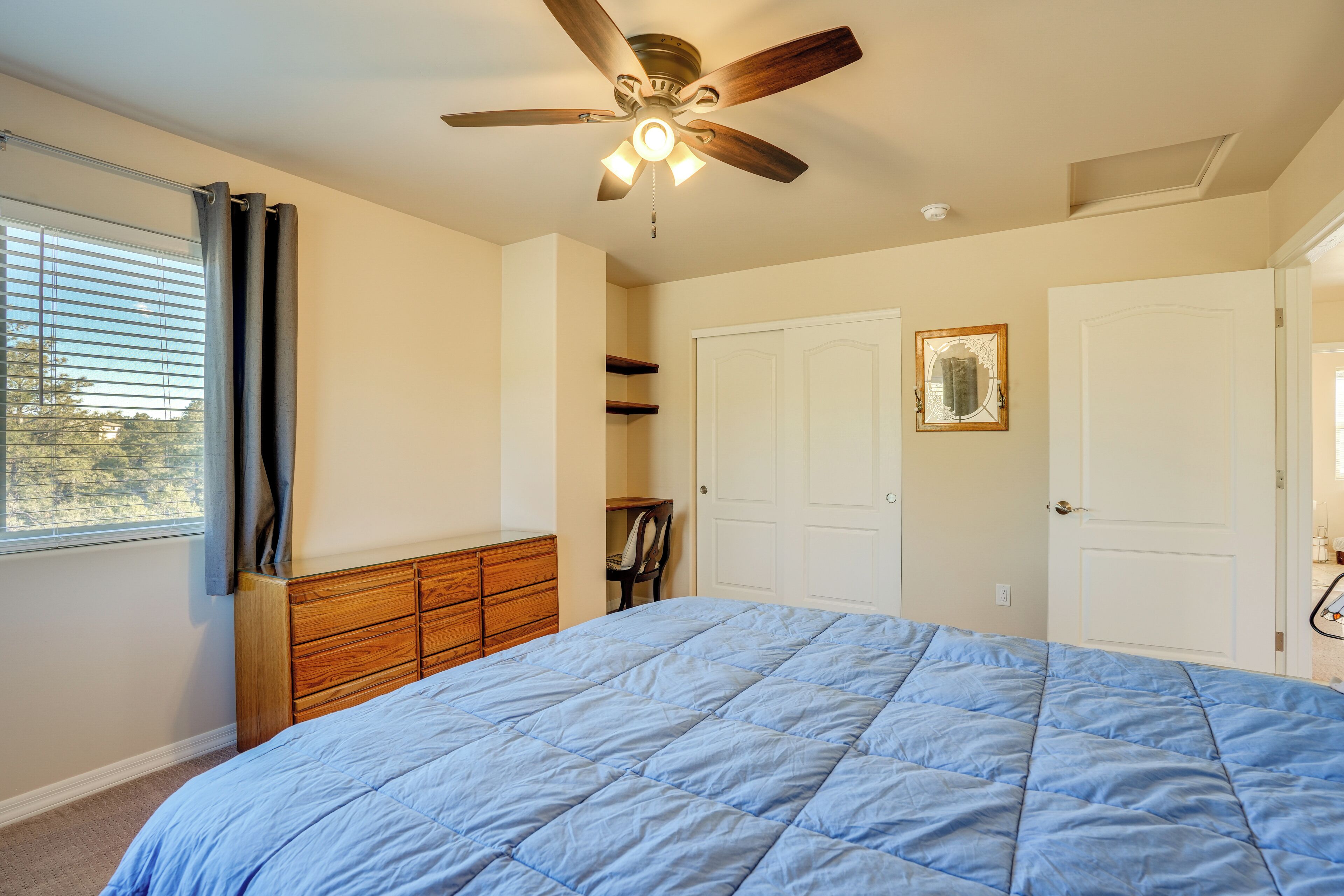 Ein Schlafzimmer mit Bett, Deckenventilator, Fenster mit Vorhängen, einem Holzschrank und weißen Türen.