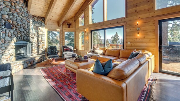 Amplia sala de estar con chimenea de piedra, sofás de cuero y grandes ventanales con vistas al exterior.