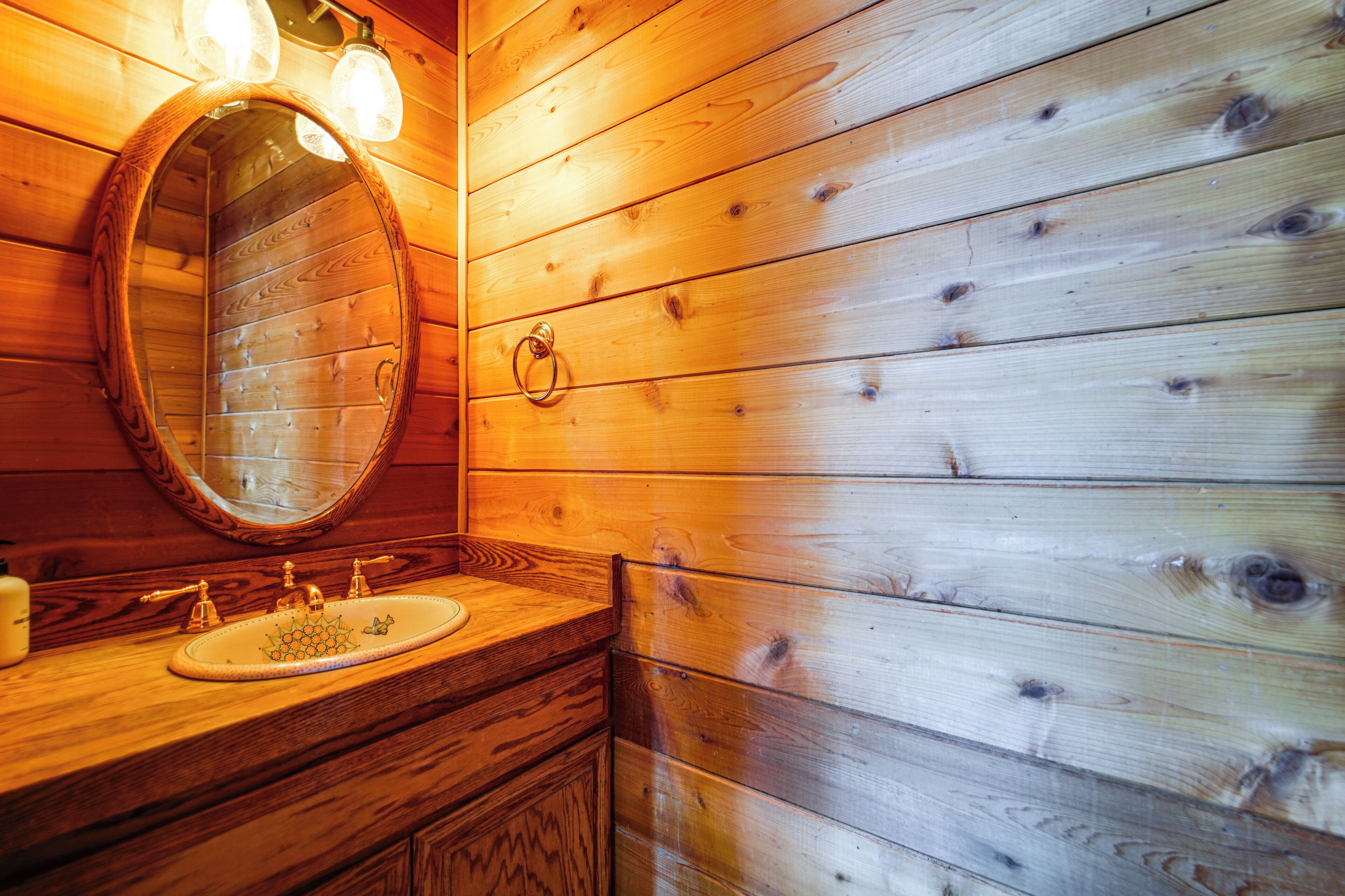 A wooden bathroom with a round mirror, a sink, and a towel ring.