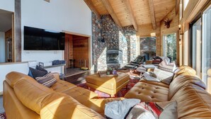 Amplia sala de estar con sofás de cuero, chimenea de piedra y un televisor grande.