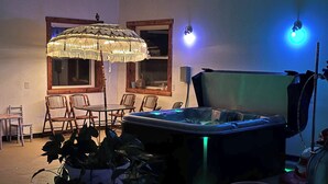 Ett rum med ett bubbelbadkar, trästolar, ett bord och ett stort parasoll.