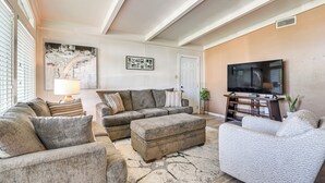 A living room with a sectional sofa, ottoman, and a flat-screen TV. - 5 Mi to Texas City Dike & Beach! Family Hideaway (Texas City)