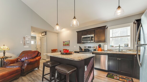 A modern kitchen with dark cabinetry, stainless steel appliances, and a central island with bar stools. - Ski, Hike & Boat: Modern Bridgton Retreat (Bridgton)