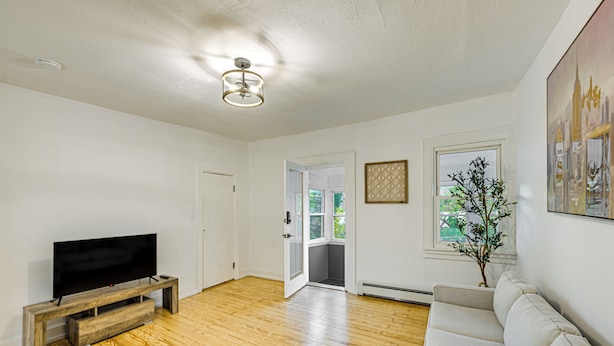 A spacious living room with a flat-screen TV on a wooden stand, a beige sofa, and a wooden floor. - NYC Area Apartment on Hudson River! (Hastings-On-Hudson)