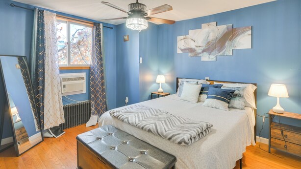 Un dormitorio con cama, lámparas de noche, ventilador de techo y ventana con cortinas.