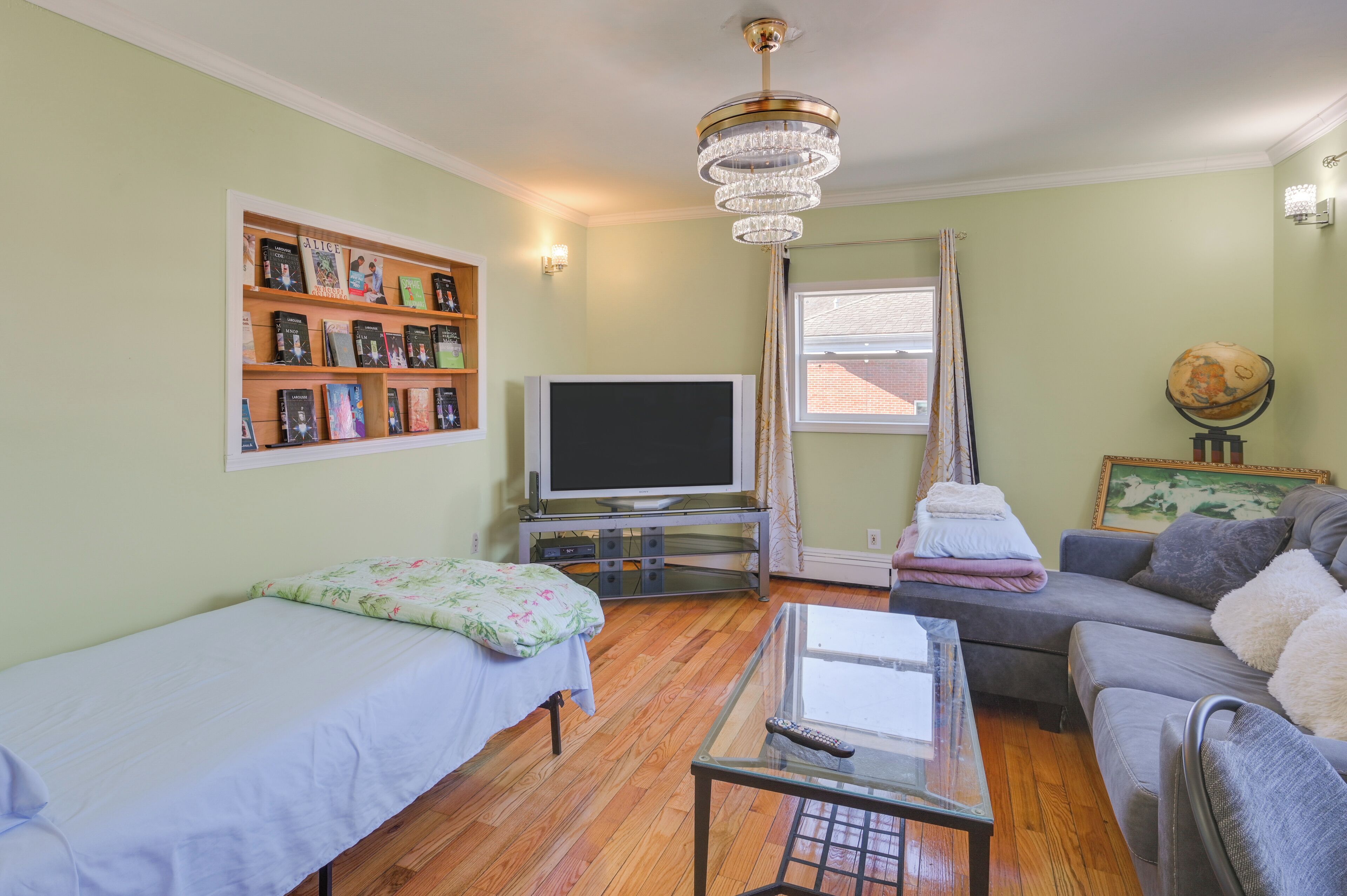 A room with a bed, a sofa, a TV, a bookshelf, and a globe.