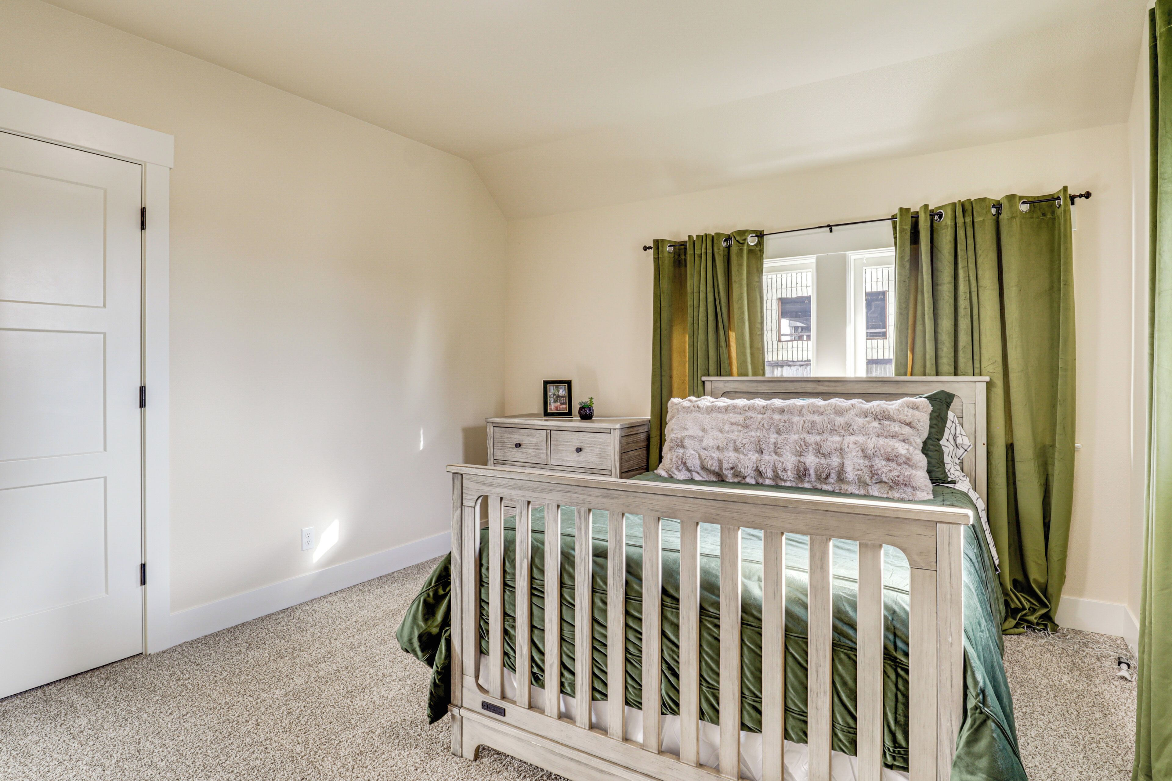 A bedroom with a crib, a nightstand, a dresser, and a window with curtains.