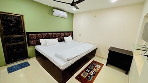 Quarto de hotel com cama, ventilador de teto, aparelho de ar condicionado, secretária pequena e tapete decorativo.