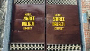 Entrada de hotel com duas grandes portas de metal com a inscrição 'HOTEL SHREE BALAJI COMFORT'.