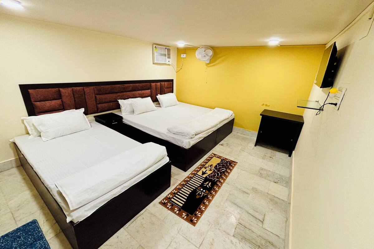 A hotel room with two beds, a small desk, a wall-mounted TV, and a ceiling fan.