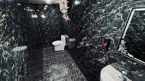Casa de banho com paredes e chão em mármore preto, sanita branca, lavatório com espelho e chuveiro manual.