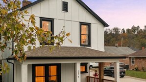 Une maison à deux étages avec un porche, une cheminée en briques et un petit jardin.