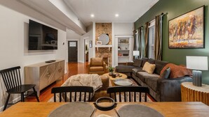 Un salon spacieux avec une cheminée, un coin repas avec une table en bois et un grand tableau accroché au mur.