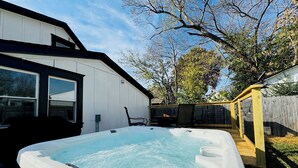Un bain à remous dans un jardin, avec une terrasse en bois, une chaise et un foyer.