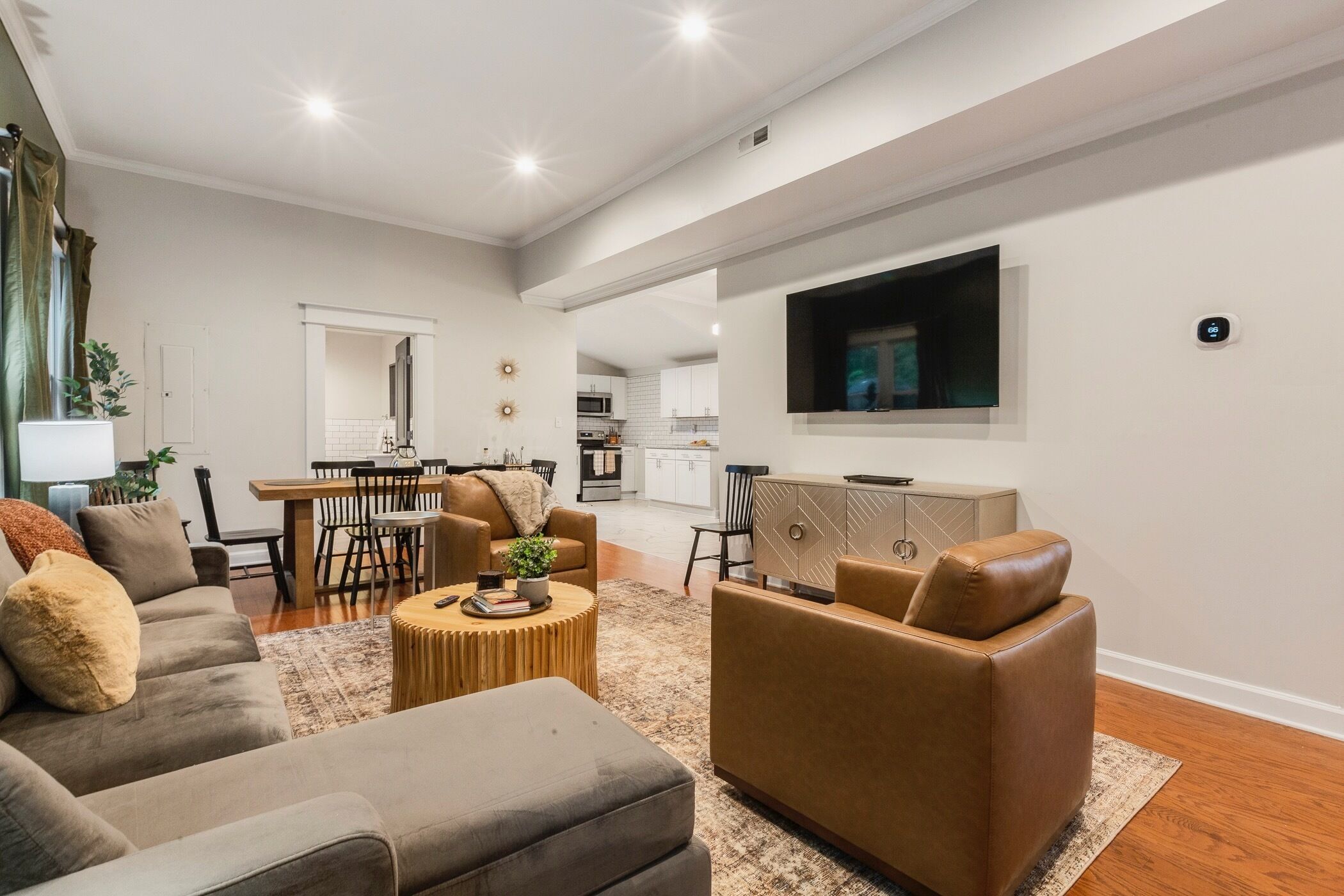 A modern living room with a sofa, armchairs, a coffee table, and a TV mounted on the wall.