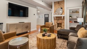 Un salon moderne doté d’un téléviseur à écran plat, de canapés en cuir, d’une table basse en bois et d’une cheminée en briques.