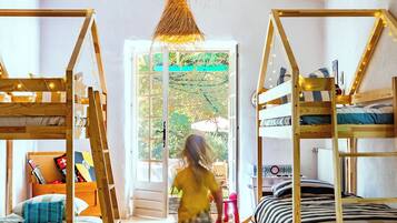 Une chambre d’enfant avec des lits superposés, une table en bois et un luminaire suspendu.