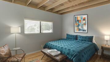 A bedroom with a bed, a bench, a chair, a window, and a painting on the wall.