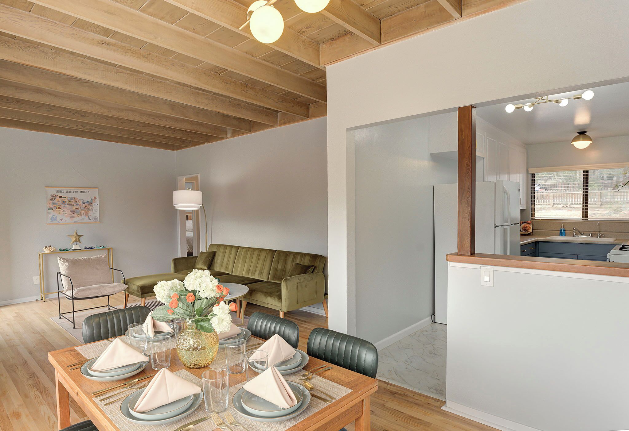 A dining area with a wooden table set for four, a green sofa, and a kitchen visible through an open doorway.