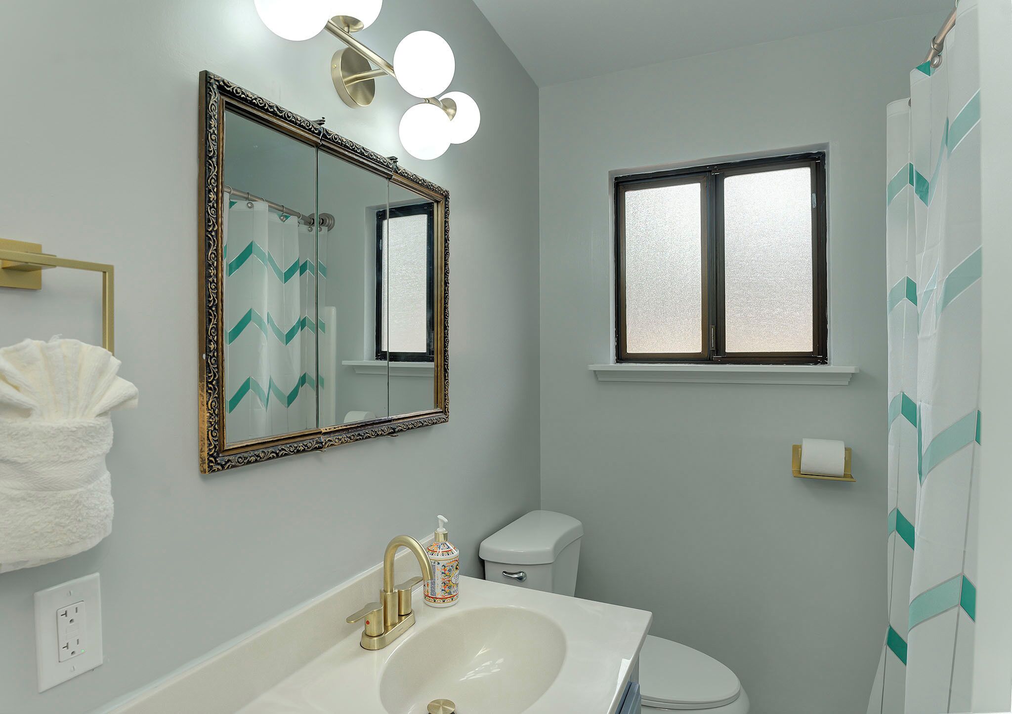 A bathroom with a large mirror, a sink, a toilet, and a window.