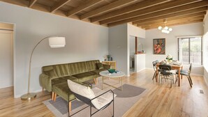 A modern living room with a green sofa, a round coffee table, and a dining area with a wooden table and chairs. - 3956 La Casa de Estrella Marie - Backyard Games! (Del Rey Oaks)