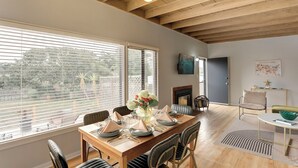 A dining area with a wooden table set for six, surrounded by upholstered chairs. There is a fireplace and a wall-mounted TV. - 3956 La Casa de Estrella Marie - Backyard Games! (Del Rey Oaks)