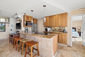 A modern kitchen with granite countertops, wooden cabinets, and bar stools. - Your Perfect Ocean View Retreat in a Desirable Location! -Kamaole Nalu #405: (Kihei, Maui)